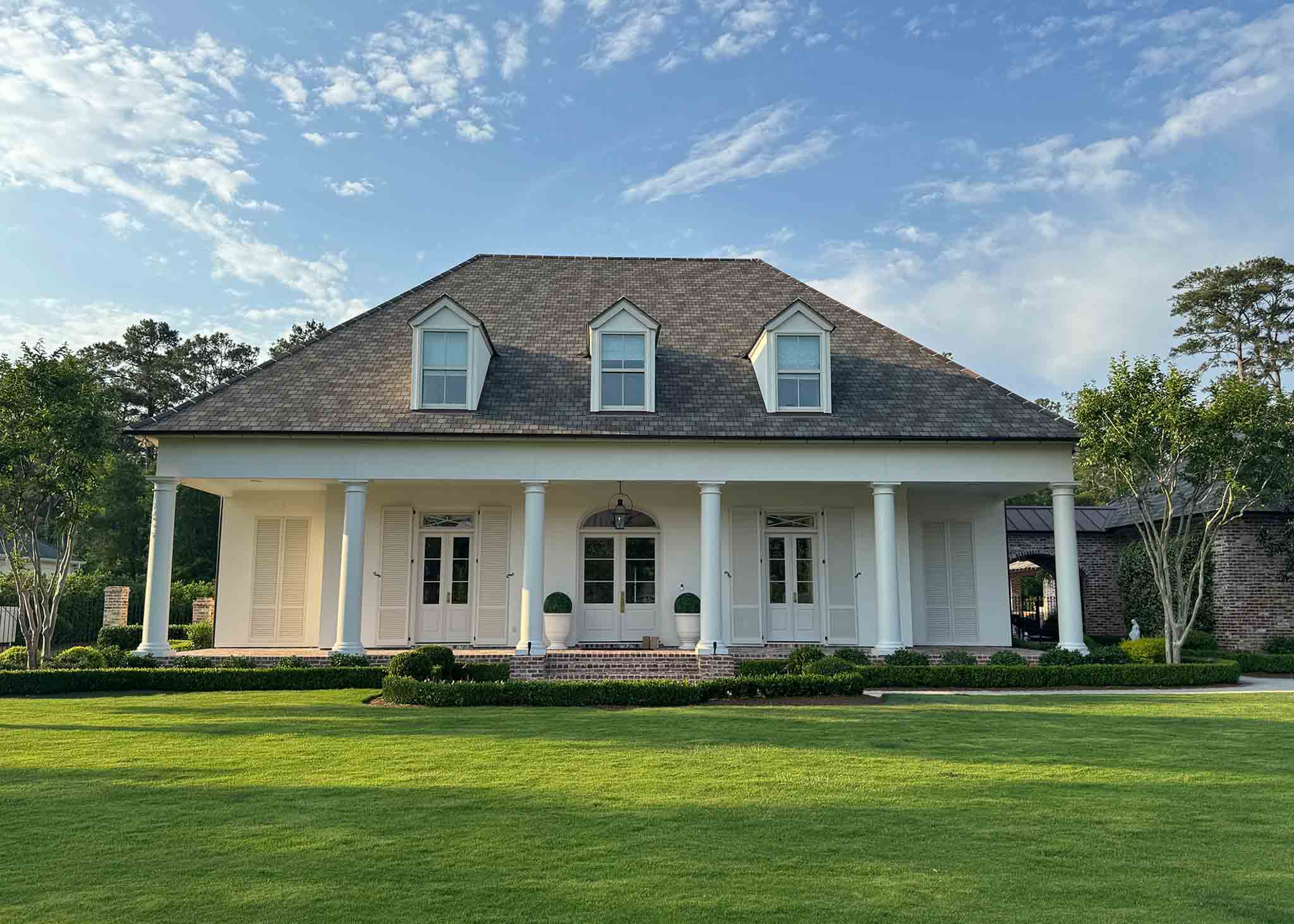 Front View of a white colonial home with manicured lawn and greenery.